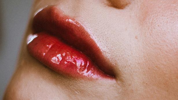 Nahaufnahme glänzend geschminkter Lippen mit rötlichem Lipgloss.