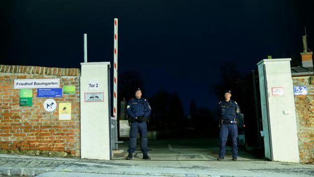 Zwei Polizisten stehen vor einem Friedhofstor.