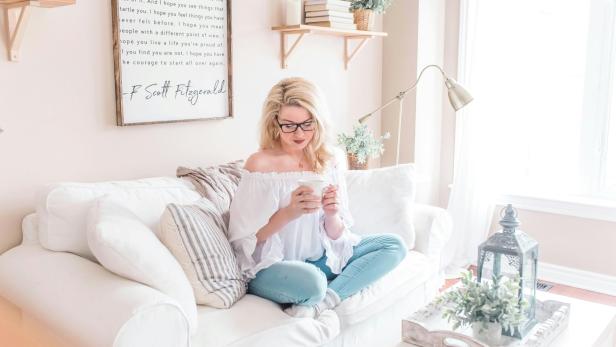 Frau sitzt auf weißer Couch, Raum ist hell beleuchtet