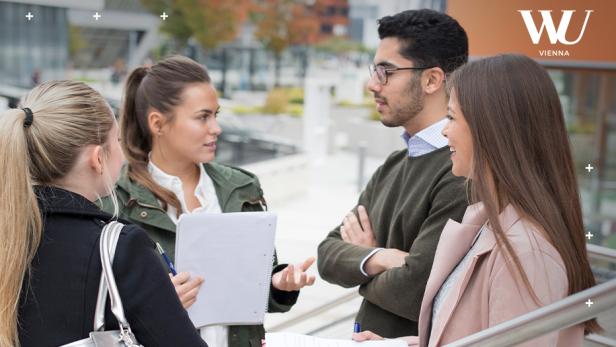 Vier junge Menschen unterhalten sich mit Notizblöcken auf dem Campus der WU Wien.