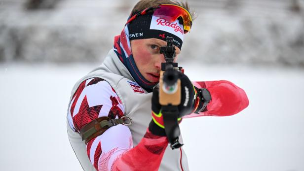 Para-Biathlet Stefan Egger-Riedmüller zielt mit einem Gewehr im Schnee, trägt Sportkleidung und eine bunte Skibrille.