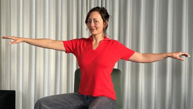 Hannah Molcar sitzt auf einem Sessel und zeigt eine Yoga-Übung vor.