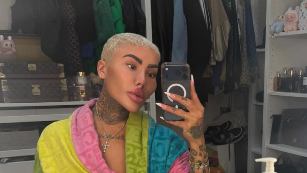 Jordan James Parke sitzt in einem bunten Bademantel vor einem Schminktisch und macht ein Selfie im Spiegel.