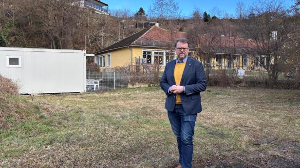 Florian Kamleitner steht vor dem Kindergarten und einer Containerklasse auf einer braun-grünen Wiese.