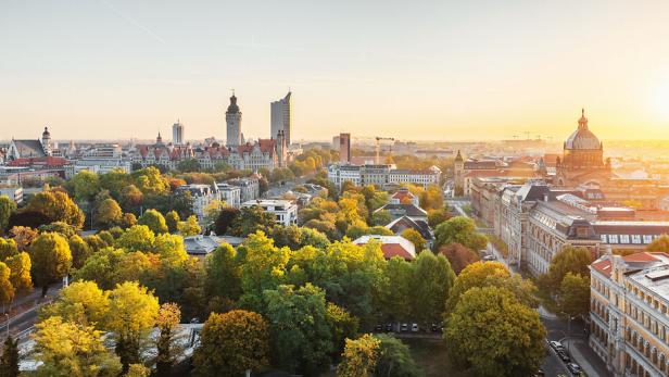Die Skyline von Leipzig mit ihren Türmen und grünen Bäumen im goldenen Licht.