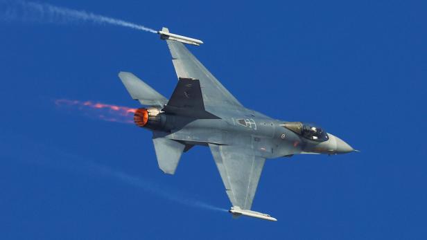 Ein Kampfjet fliegt mit Nachbrenner und Kondensstreifen durch den klaren blauen Himmel.