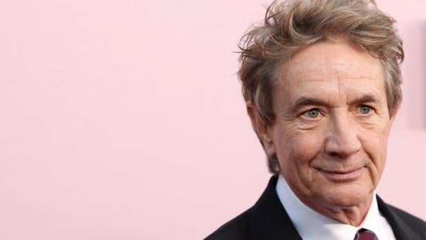 Martin Short lächelt vor einem hellrosa Hintergrund in die Kamera.