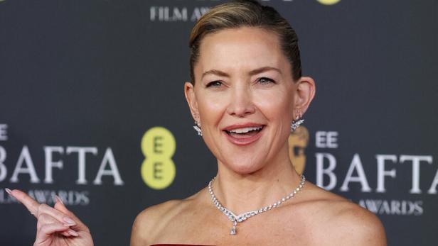 Kate Hudson in einem roten, schulterfreien Kleid und Schmuck auf dem roten Teppich der BAFTA Film Awards.