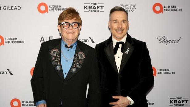 Elton John und David Furnish halten Händchen auf einem Event.