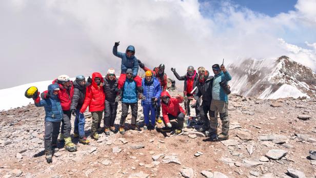 Gruppe von Bergsteigerinnen und Bergsteigern in Winterkleidung am schneebedeckten Gipfel.