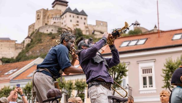 Zwei Musiker mit fantasievollen Kostümen spielen Trompete vor einer Burg und begeistern das Publikum.