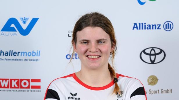 Veronika Aigner: Junge Frau mit verschränkten Armen im Sporttrikot steht vor einer Sponsorenwand und lächelt.