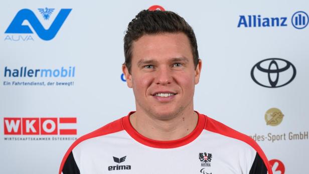 Stefan Winter: Ein Mann mit kurzem dunklem Haar trägt ein weißes Sportshirt mit roten Akzenten und steht vor einer Sponsorenwand.