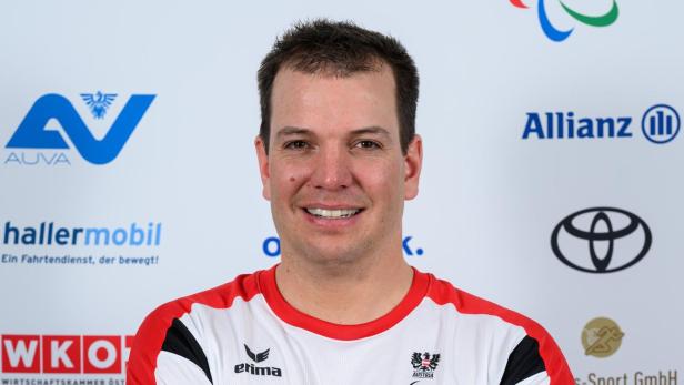 Markus Salcher: Ein Mann mit kurzem Haar trägt ein rot-weißes Sporttrikot und steht mit verschränkten Armen vor einer Sponsorenwand.