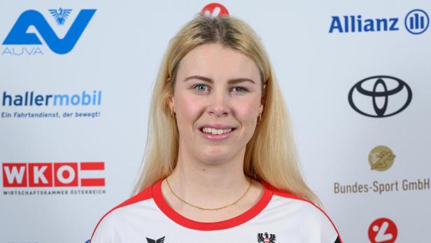 Laura Streng : Junge Frau mit langen blonden Haaren trägt ein österreichisches Sporttrikot und steht vor einer Sponsorenwand.