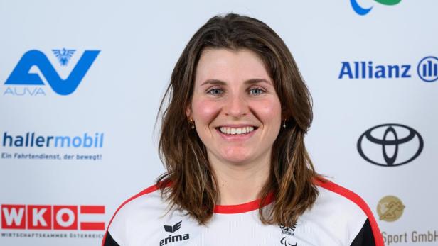 Elisabeth Aigner: Eine Frau mit schulterlangem braunem Haar trägt ein weiß-rotes Sporttrikot und steht lächelnd vor Sponsorenlogos.