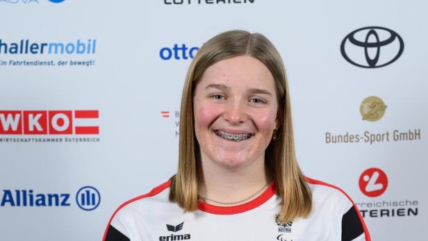Lilly Sammer: Junge Frau mit schulterlangem blondem Haar trägt ein österreichisches Sporttrikot und lächelt vor einer Sponsorenwand.