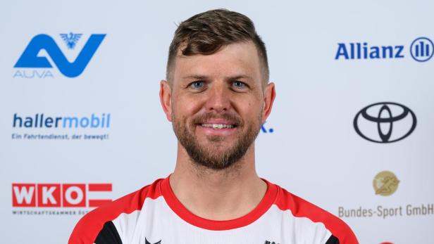 Rene Eckhart: Ein Mann im weißen Sporttrikot mit roten Akzenten steht lächelnd mit verschränkten Armen vor Sponsorenlogos.