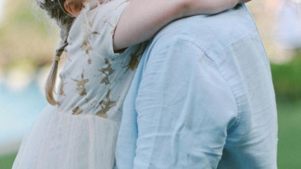 Ein Mädchen mit Zöpfen umarmt einen Erwachsenen im Freien.