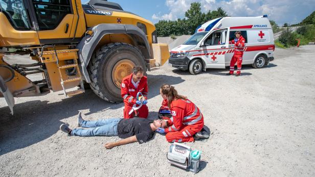Zwei Sanitäter verarzten einen Mann am Boden vor einem gelben Fahrzeug. Es ist eine Übung.