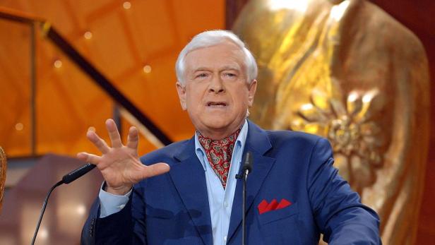 Hademar Bankhofer mit blauem Sakko gestikuliert vor einem Mikrofon auf einer Bühne.