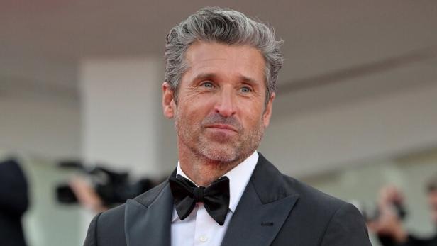 Patrick Dempsey trägt einen schwarzen Smoking mit Fliege und hält eine Brille in der Hand.