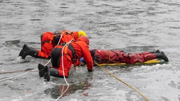 Zwei Feuerwehrmänner ziehen eine Person aus dem Eis.