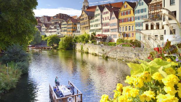 Bunte Fachwerkhäuser am Flussufer, Stocherkahn mit Menschen auf dem Wasser, sonniger Tag.