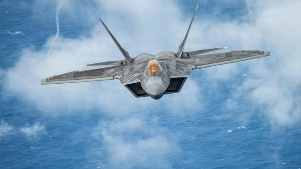 Ein F-22-Kampfjet fliegt über Wolken und Ozean in Richtung Kamera.