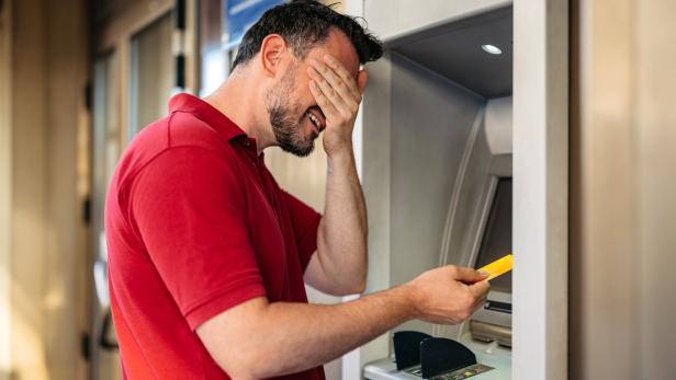 Mid-Adult Man Covering His Eyes Before Withdrawing Money Using A Credit Card At The ATM Machine