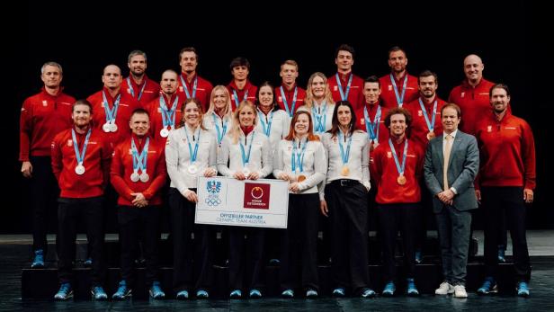 Eine große Gruppe von Sportlerinnen und Sportlern mit Medaillen steht gemeinsam auf einer Bühne und lächelt.