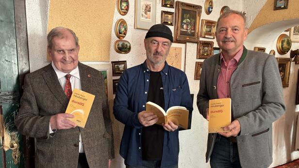 Drei Männer präsentieren das Buch "durstIG" von Martin Franz Neuberger vor einer Wand mit Bildern.