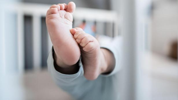 Ein Baby liegt im Gitterbett und streckt seine Füße in die Luft.