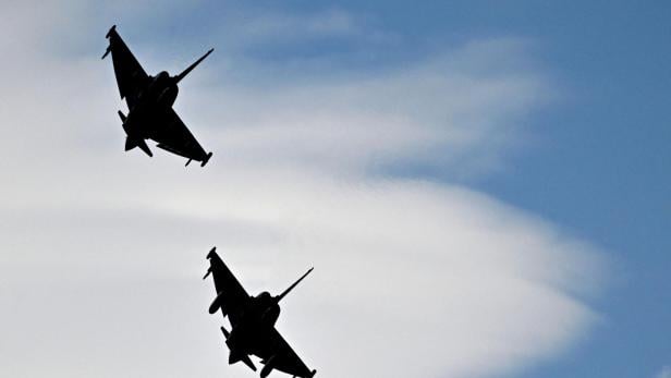 Zwei Kampfjets fliegen nebeneinander am Himmel vor weißen Wolken.