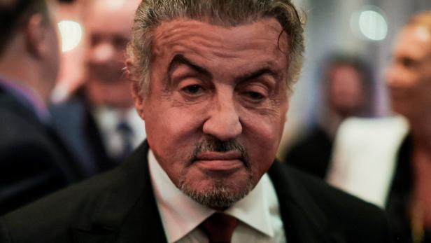 Sylvester Stallone mit Anzug und Bart blickt ernst in die Kamera.