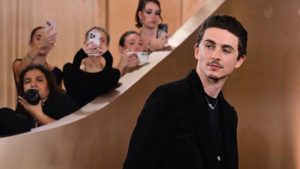 Timothée Chalamet blickt ernst drein, umringt von Menschen bei einem öffentlichen Event