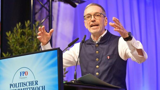 Ein Mann, es ist Herbert Kickl, mit Brille gestikuliert am Rednerpult vor einem Bildschirm mit FPÖ-Logo.
