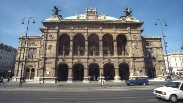 Prächtiges historisches Gebäude mit Arkaden, Statuen und Kuppel, davor fahren Autos und gehen Menschen entlang der Straße.