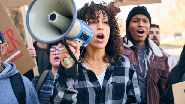 Diverse group of people holding signs as a woman speaks through a megaphone at a positive community rally