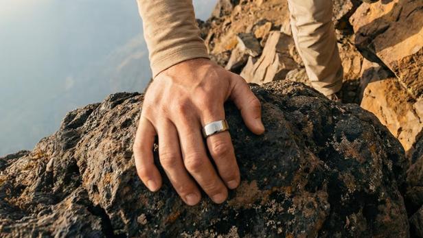 ein Mann in beigem Outfit klettert auf einen Berg, an der Hand hat er einen silberenen Ring
