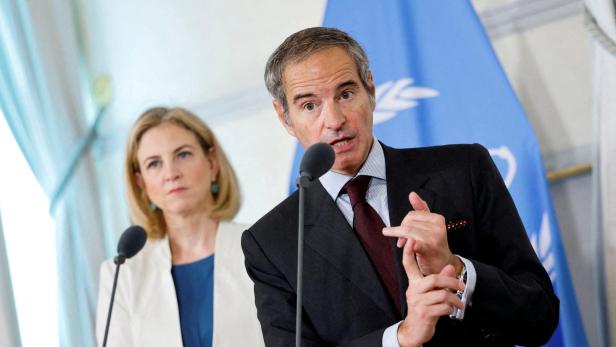 Ein Mann im Anzug spricht gestikulierend am Mikrofon, eine Frau steht im Hintergrund neben ihm.