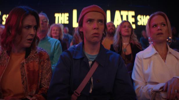 Eine Szene aus "How To Get To Heaven From Belfast": Saoirse, Dara und Robyn sitzen im Publikum einer Late-Night-Show.