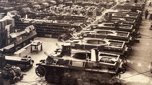 Mehrere Panzer werden in einer großen Fabrikhalle in verschiedenen Bauphasen montiert.