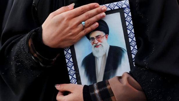 Eine Person hält ein gerahmtes Porträt von Ali Khamenei an ihre Brust.