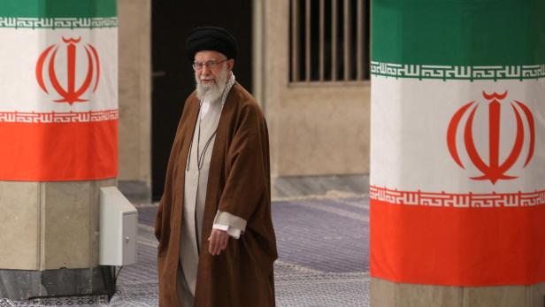 Ali Khamenei geht an Säulen mit iranischen Flaggen vorbei.
