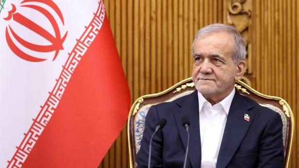 Ein Mann im Anzug sitzt neben der iranischen Flagge.