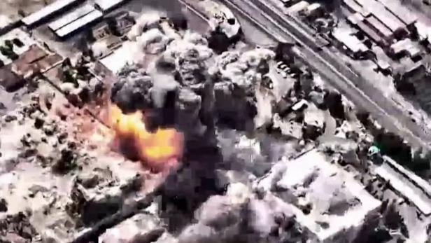 Eine Explosion hüllt Gebäude in Rauch und Feuer, aufgenommen aus der Luft.