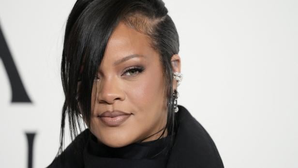 Rihanna blickt mit dunklem Haar und auffälligem Ohrschmuck in die Kamera.