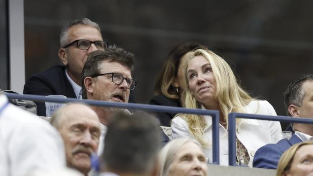 Michael J. Fox und Tracy Pollan sitzen nebeneinander auf einer Tribüne und schauen aufmerksam in eine Richtung.