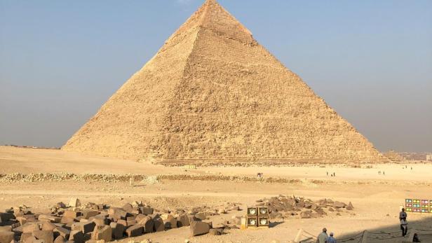 Pyramide in der Wüste mit mehreren Touristen im Vordergrund bei klarem Himmel.